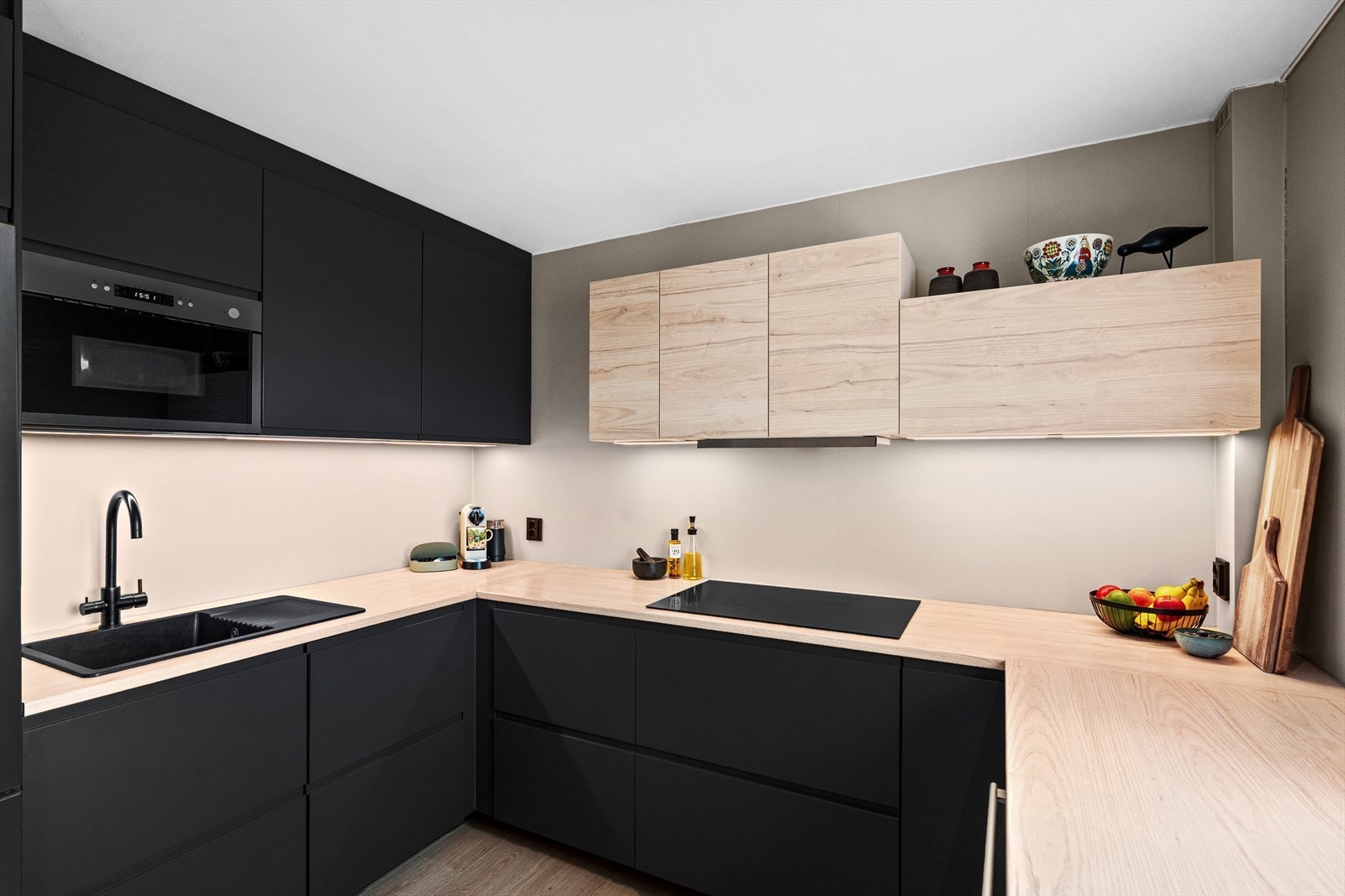 Kjøkkenet er fra IKEA med grå, matte fronter og i lyse tretoner. Det er benkeplater i laminat, sort oppvaskkum og ventilator. Galleribilde