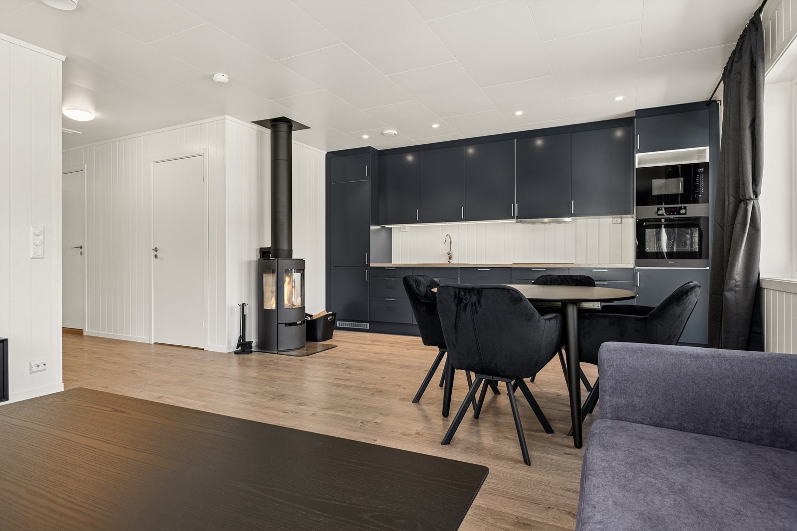 Den åpne planløsningen gir en god romfølelse og binder de ulike sonene sammen. Overflater er utført med malte panelplater på vegger og laminatgulv, som gir et lyst, moderne og enhetlig preg. Galleribilde