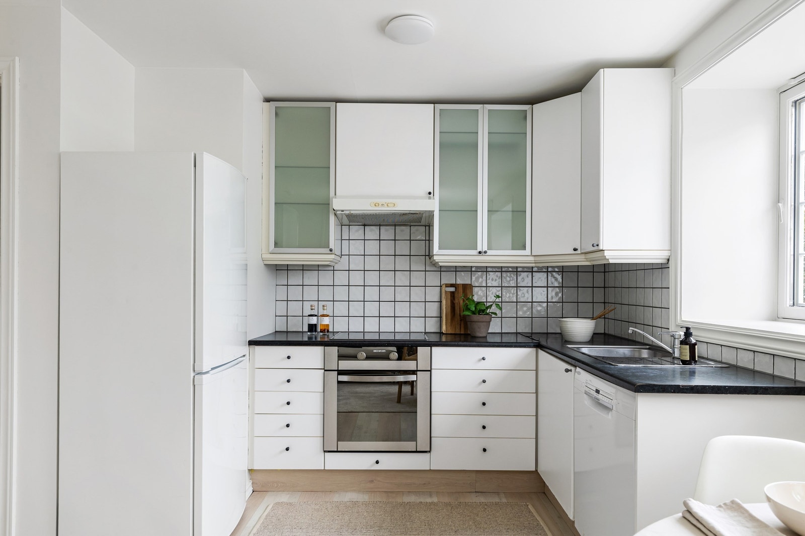 Praktisk kjøkken med flislagt bakvegg over benk og opplegg for oppvaskmaskin. Galleribilde