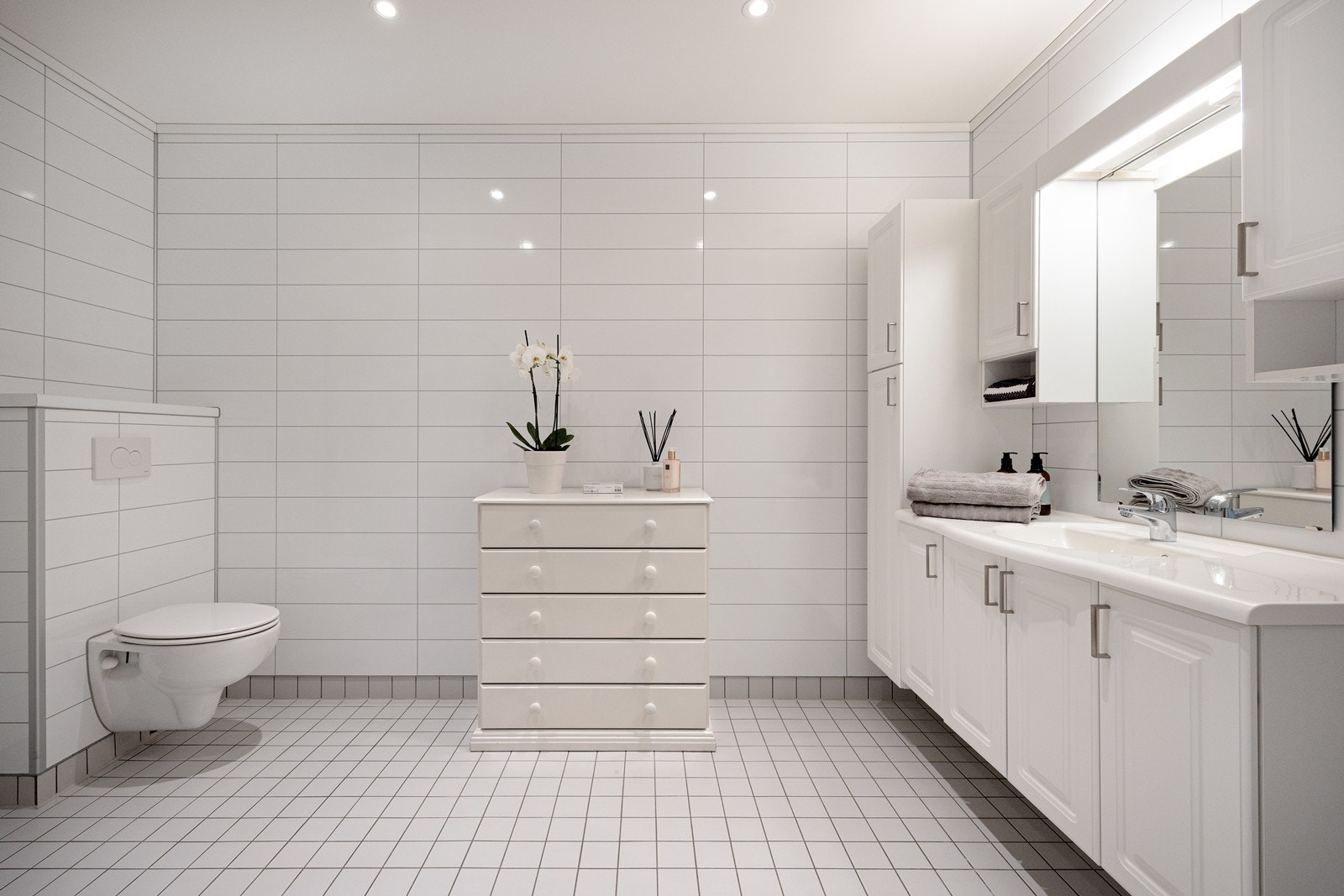 Badet fremstår som romslig, stilrent og velholdt, med downlights i himlingen og lyse fliser på gulv med gulvvarme. Galleribilde