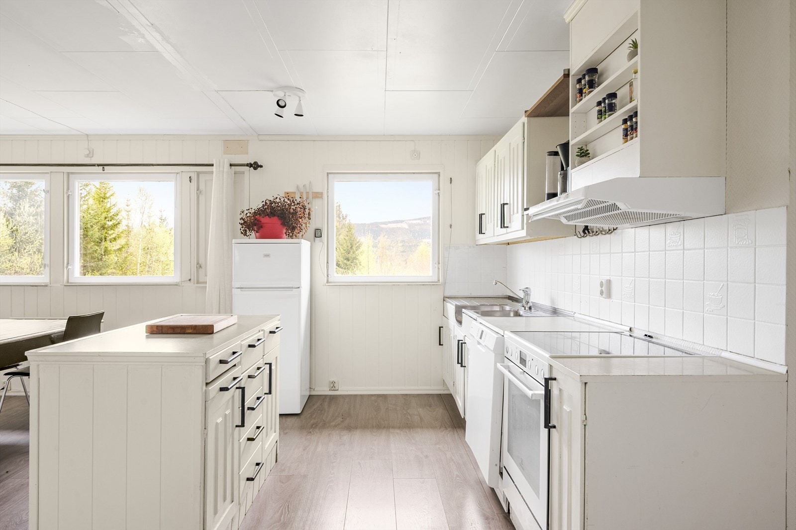 Kjøkken/spisestue har moderne enstavs laminat fra ca. 2023 på gulv, lysmalte overflater og flere store vinduer som slipper inn fint naturlig lys. Galleribilde