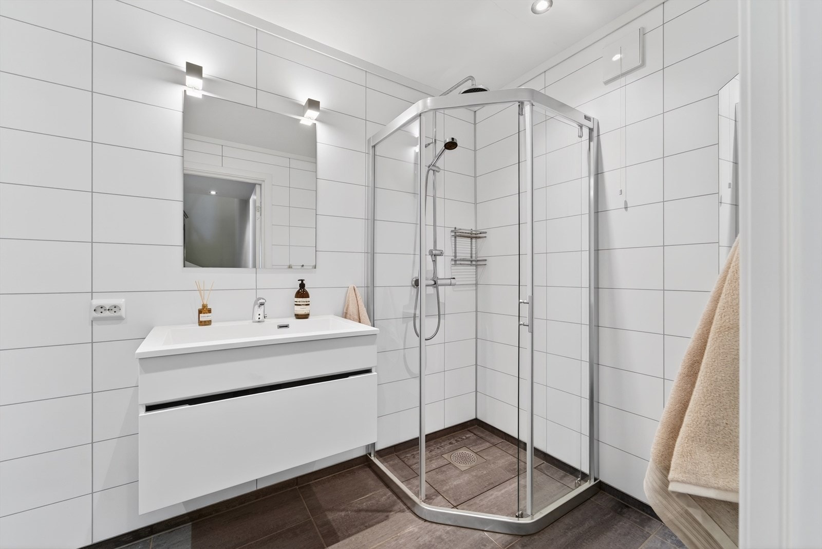 Baderom med moderne innredning, dusjkabinett og vegghengt toalett. Fliser på gulv og baderomsplater på vegg. Galleribilde