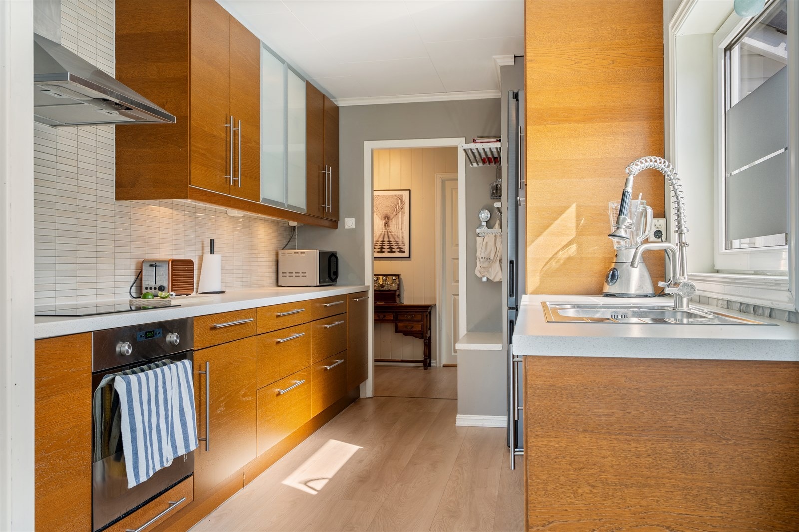Moderne kjøkken med stilren design, slette overflater og laminert benkeplate. Kjøkkenet er utstyrt med integrert induksjonstopp, stekeovn og oppvaskmaskin. Galleribilde