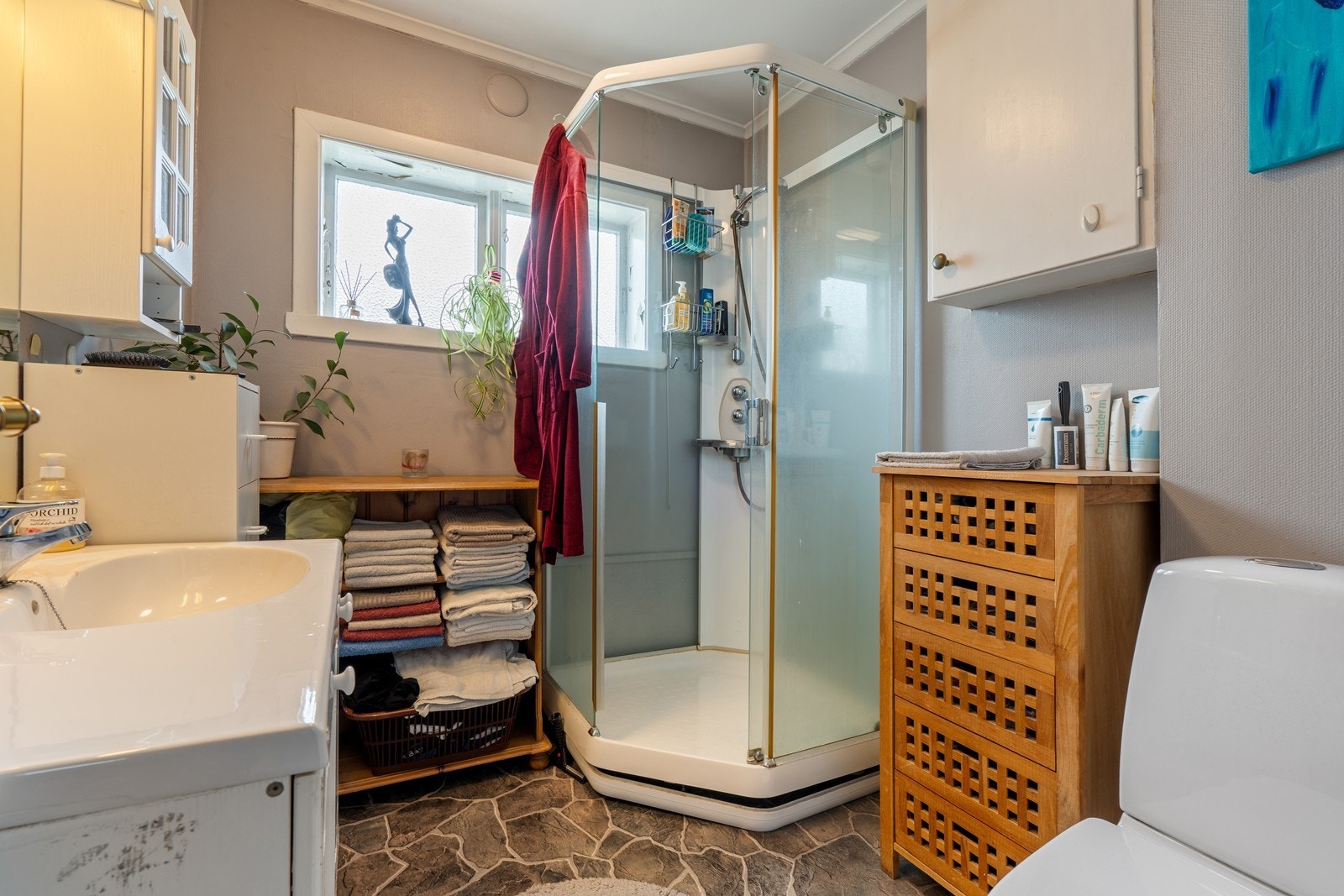 Badet i 1. etasje har vegger med malt strie og gulv med belegg - badet er innredet med hvit baderomsinnredning, gulvmontert toalett og dusjkabinett Galleribilde