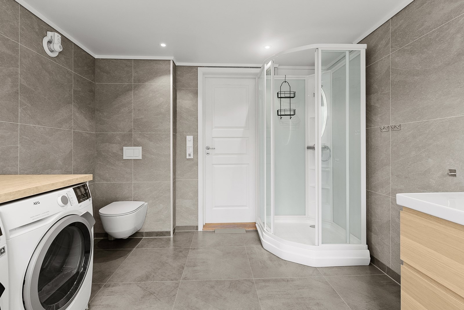 Badet inneholder servant med innredning, dusjkabinett, veggmontert wc og opplegg til vaskemaskin. Galleribilde