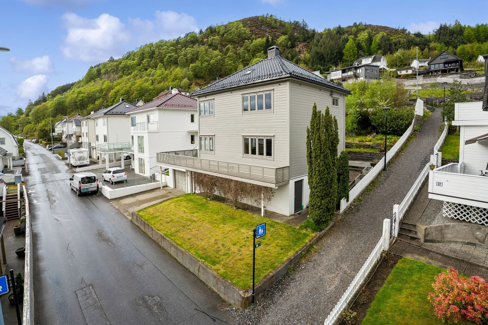 Uteområdeter pent opparbeidd med hage- og plenareal i lett skrånande terreng på baksida av bustaden, skjerma med vintergrøn hekk og rikt beplanta med prydbuskar, blomster og natursteinsmurar som skapar ei lun og innbydande ramme rundt uteområdet. Galleribilde