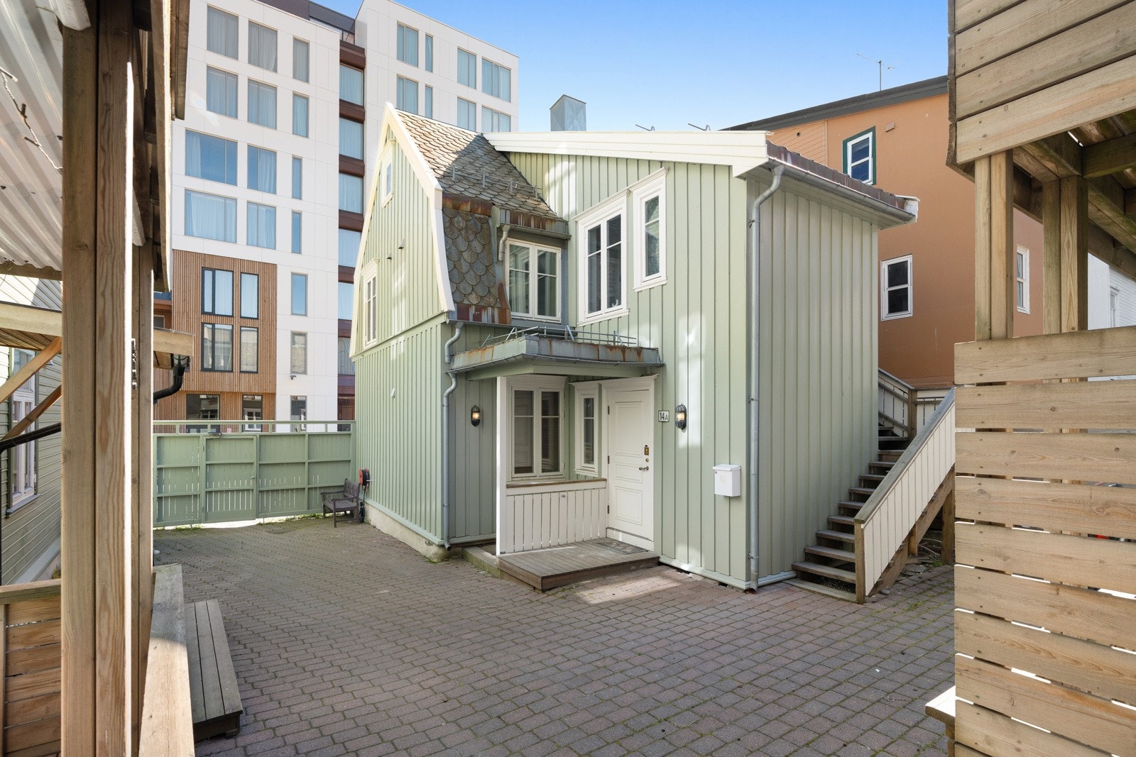 Skjermet bakgård med brostein, varmekabler og treporter mot Storgata.