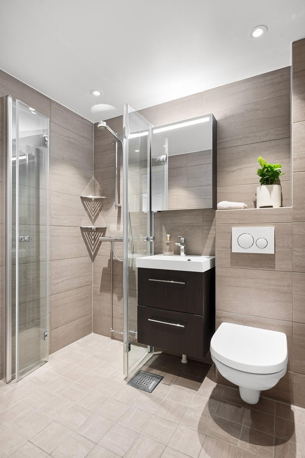 Badet er utstyrt med elektrisk gulvvarme, vegghengt toalett, servantskap med skuffeløsninger, speilskap med integrert belysning og dusjhjørne med innfellbare glassdører. Det er downlights i nedsenket himling som gir behagelig belysning. Galleribilde
