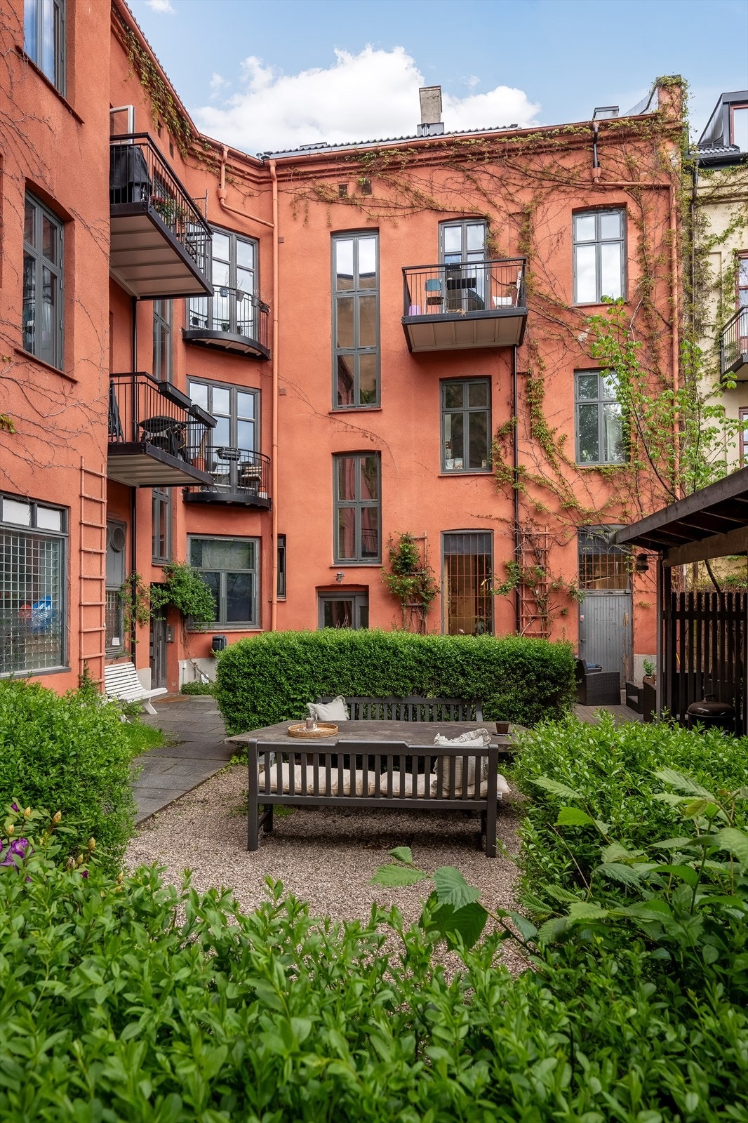 Pent opparbeidet bakgård med slyngplanter, blomsterbed, gressplen, heller, platting, sittegrupper og sykkelparkering under tak Galleribilde