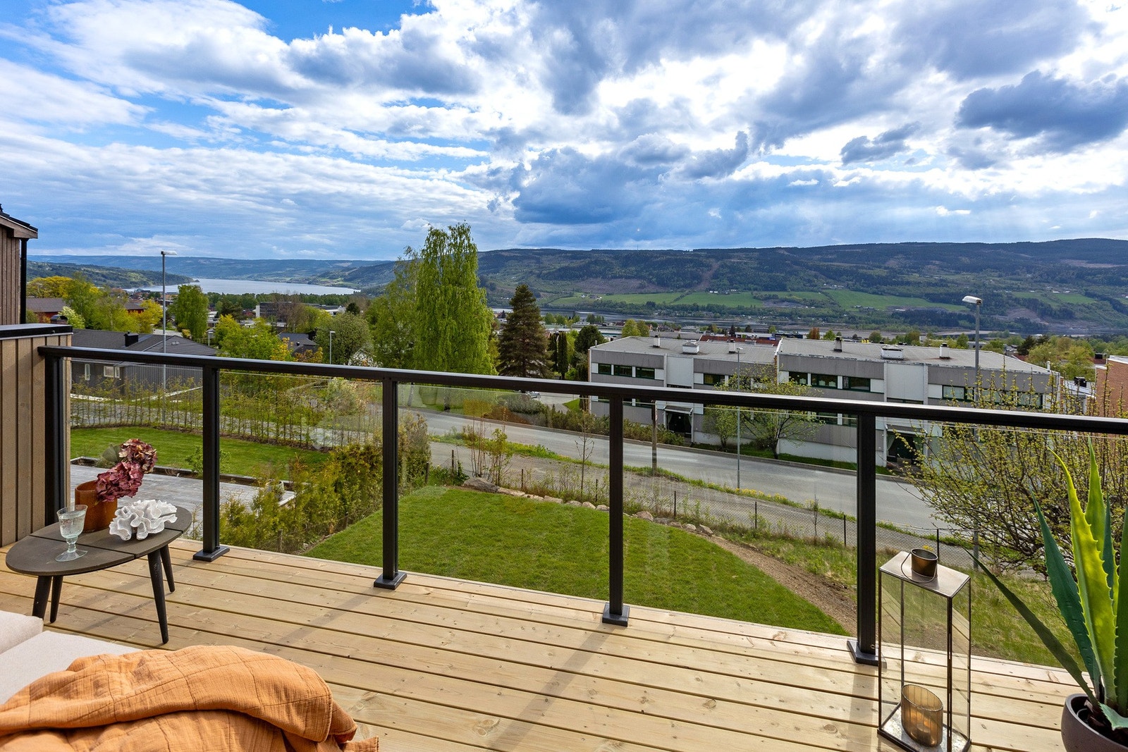 Solrik balkong med glassrekkverk og nydelig utsyn mot Mjøsa, deler av Lillehammer by og omkringliggende landskap. Galleribilde