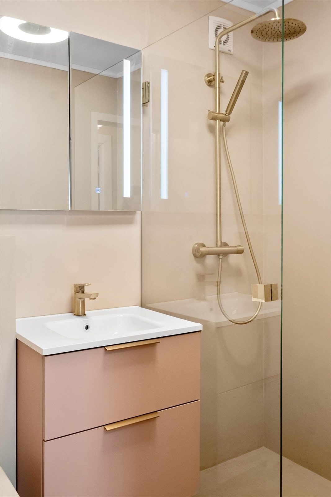 Badet er innredet med servant med underskap, veggmontert toalett og dusjhjørne med dusjvegger Galleribilde