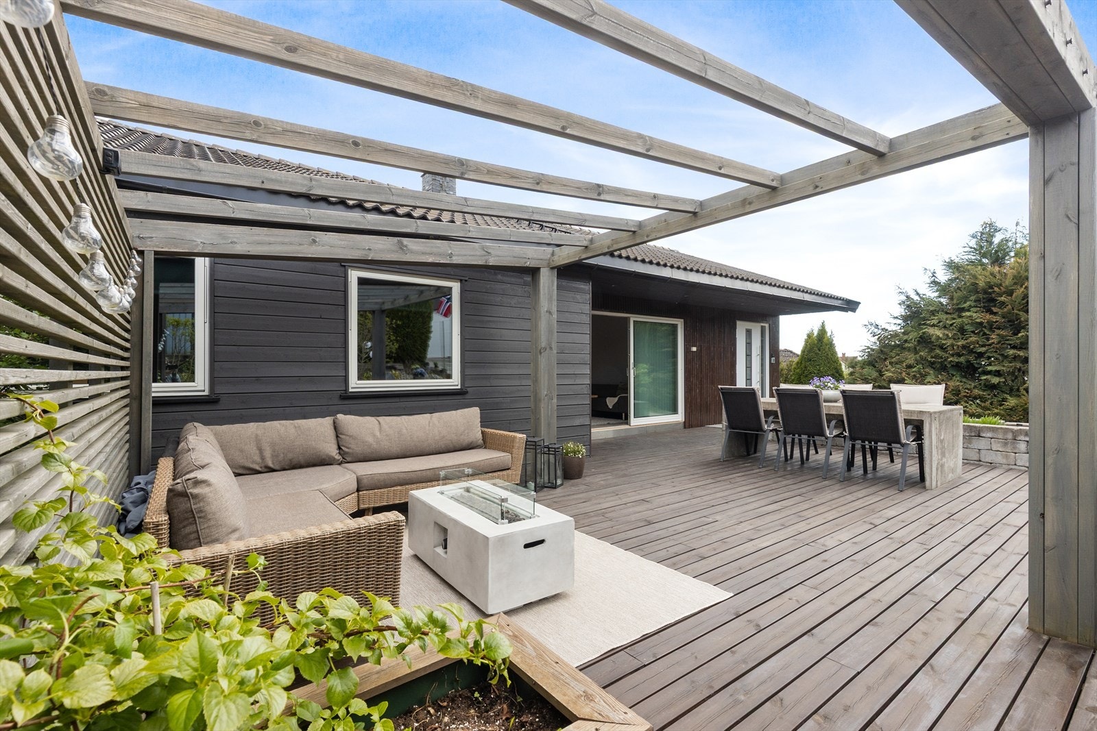 Pergola og terrasse forbinder uteområdet med stuen og hovedinngangen. Pergolaen skaper en lun og definert sone for en utendørs sofagruppe. En herlig uteplass, fri for innsyn! Galleribilde