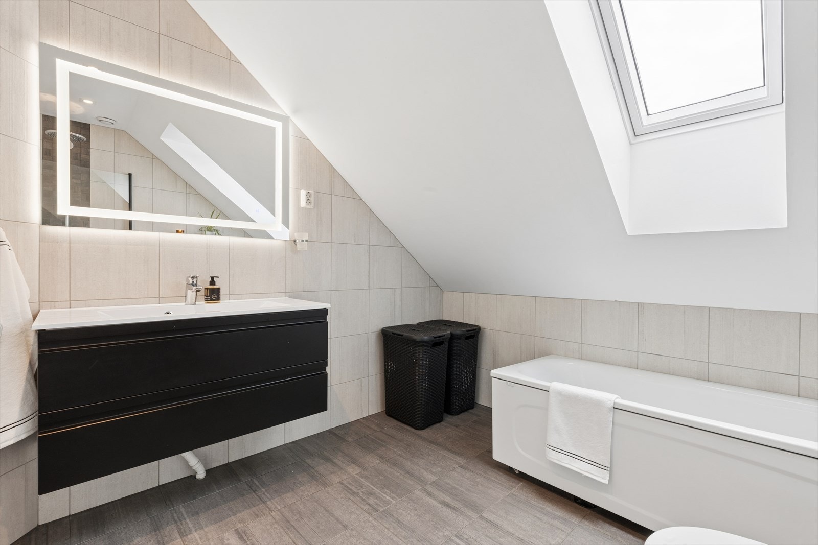 Lyst og romslig bad i andre etasje med takvindu, badekar og moderne innredning. Dette badet ble pusset opp i 2021. Galleribilde