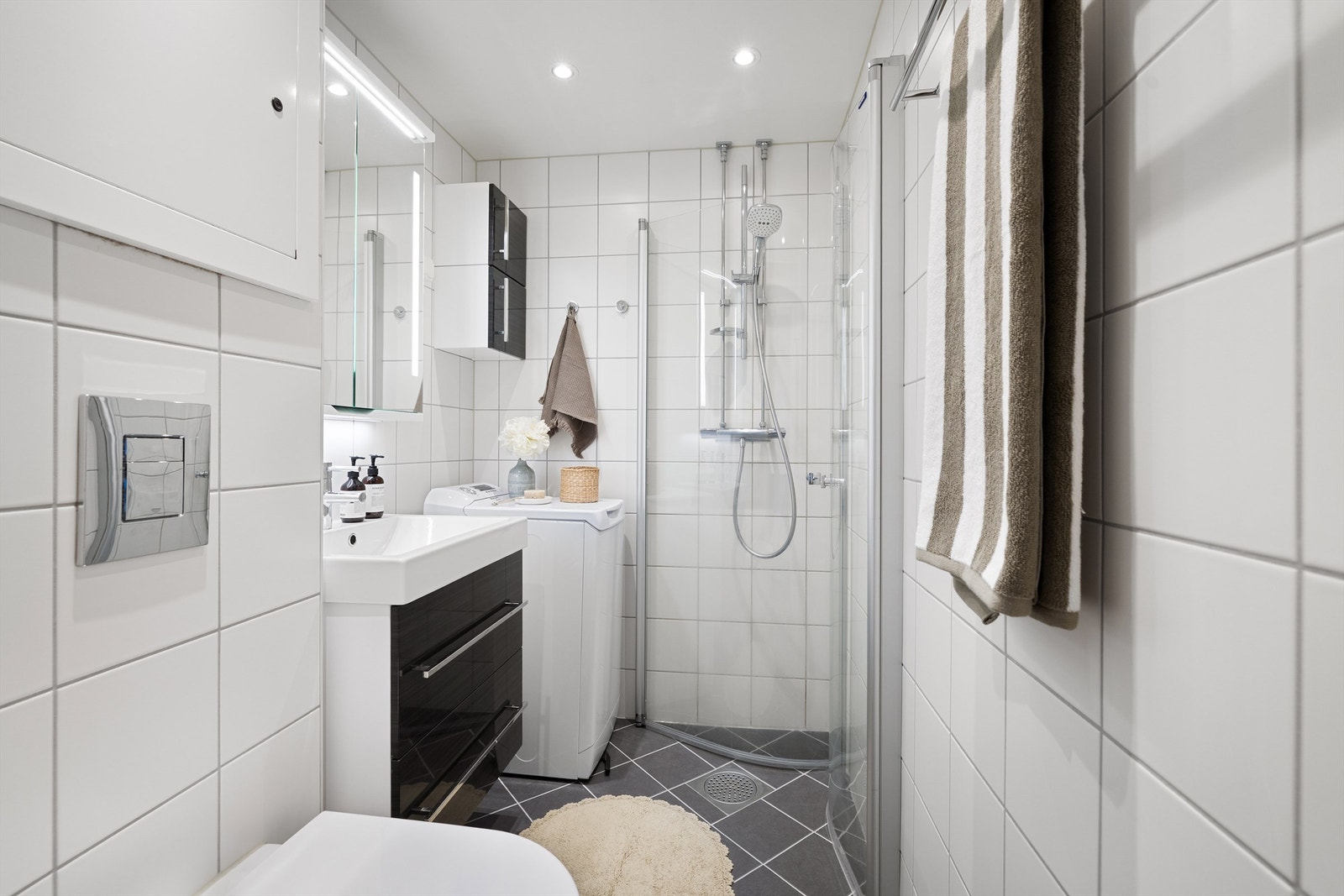 Himling med malte plater, innfelte downlights. Gulv med fliser og elektrisk gulvvarme. Innredet med vegghengt klosett, servant med innredning, speilskap med lys og dusjhjørne med svingbare glassdører. Opplegg for vaskemaskin. Mekanisk avtrekk Galleribilde