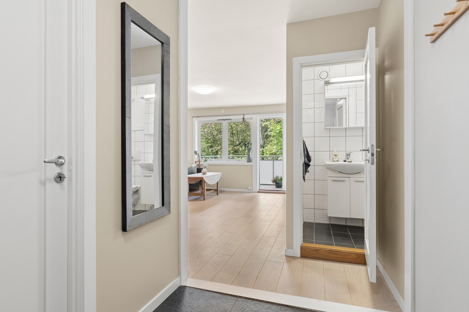 Et blikk fra entreen mot stuen og badet, som viser leilighetens gjennomgående materialvalg. Galleribilde