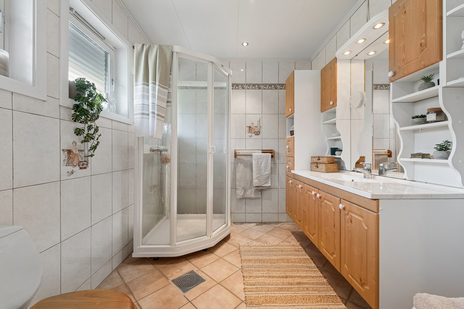 Badet i hovedetasjen er pent flislagt med varmekabler i gulvet. Innredningen består av et praktisk baderomsmøbel med skaper, speil, lys, dusjkabinett og toalett. Vaskerom og ytterligere bodplass finner du i boligens kjelleretasje. Galleribilde