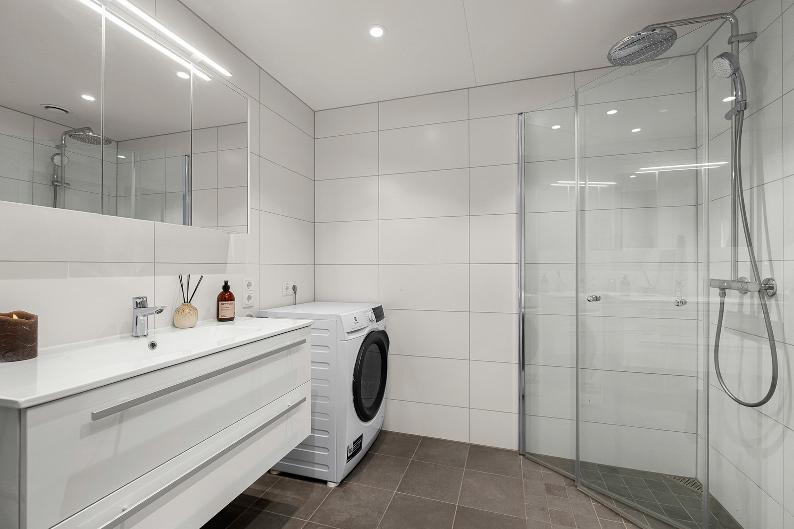 Pent flislagt bad på 5 kvm med gulvvarme, downlights i himling og opplegg for vaskemaskin. Videre er badet innredet med servantskap med speil og lys, dusjhjørne med regndusj og vegghengt toalett. Galleribilde