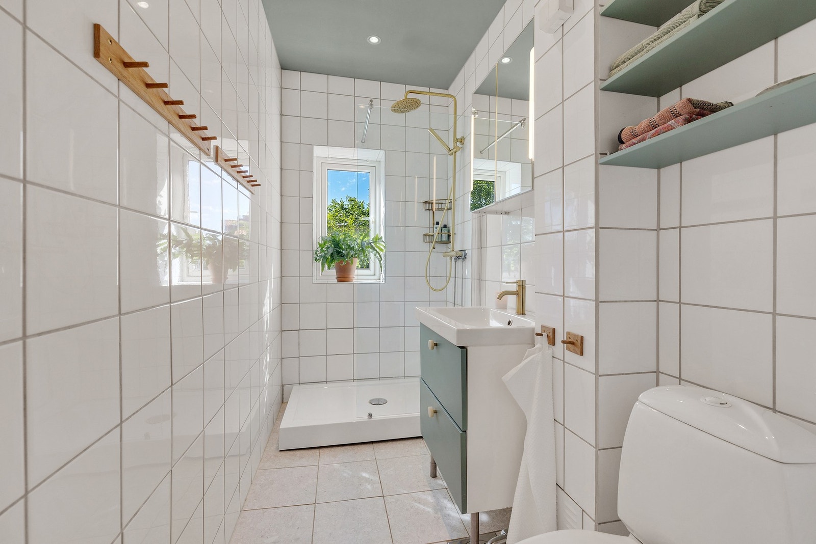 Badet har flislagte overflater og en praktisk planløsning med dusjkar og fast glassfelt, servant med oppbevaringsløsninger og veggskap med speilfronter. Galleribilde