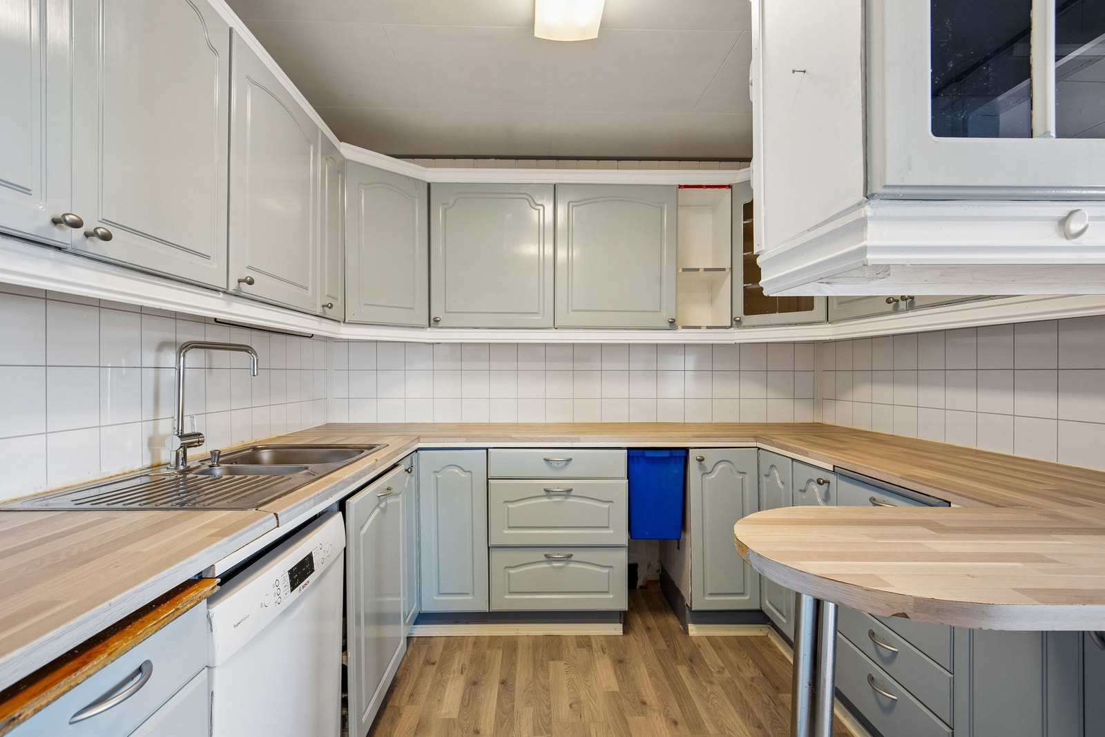 Kjøkkeninnredning med profilerte fronter og benkeplate i laminat. Det er kjøkkenventilator med avtrekk ut. Galleribilde