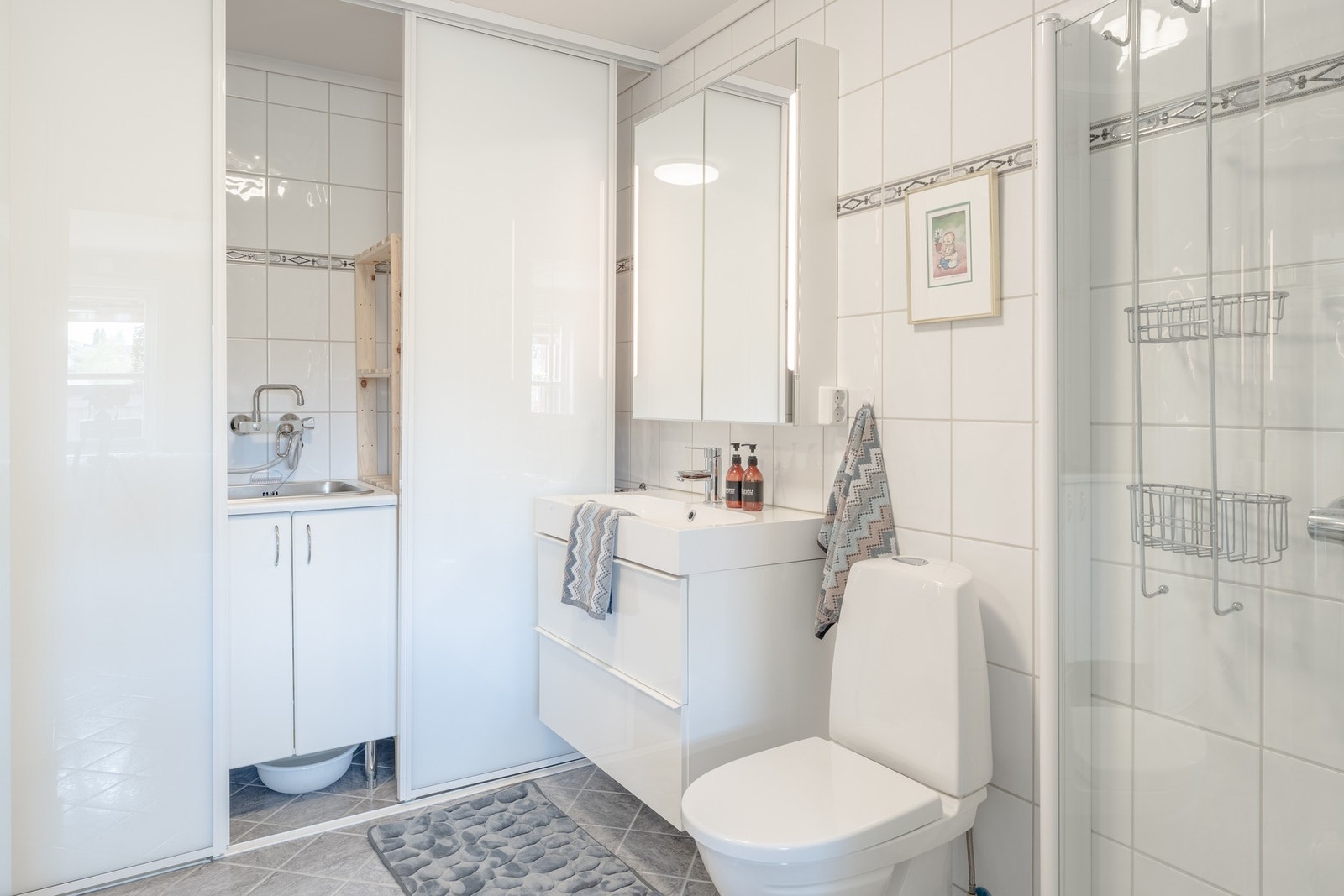Badet er innredet med toalett, dusj med glassvegger, og baderomsmøblement med speil og belysning. Galleribilde