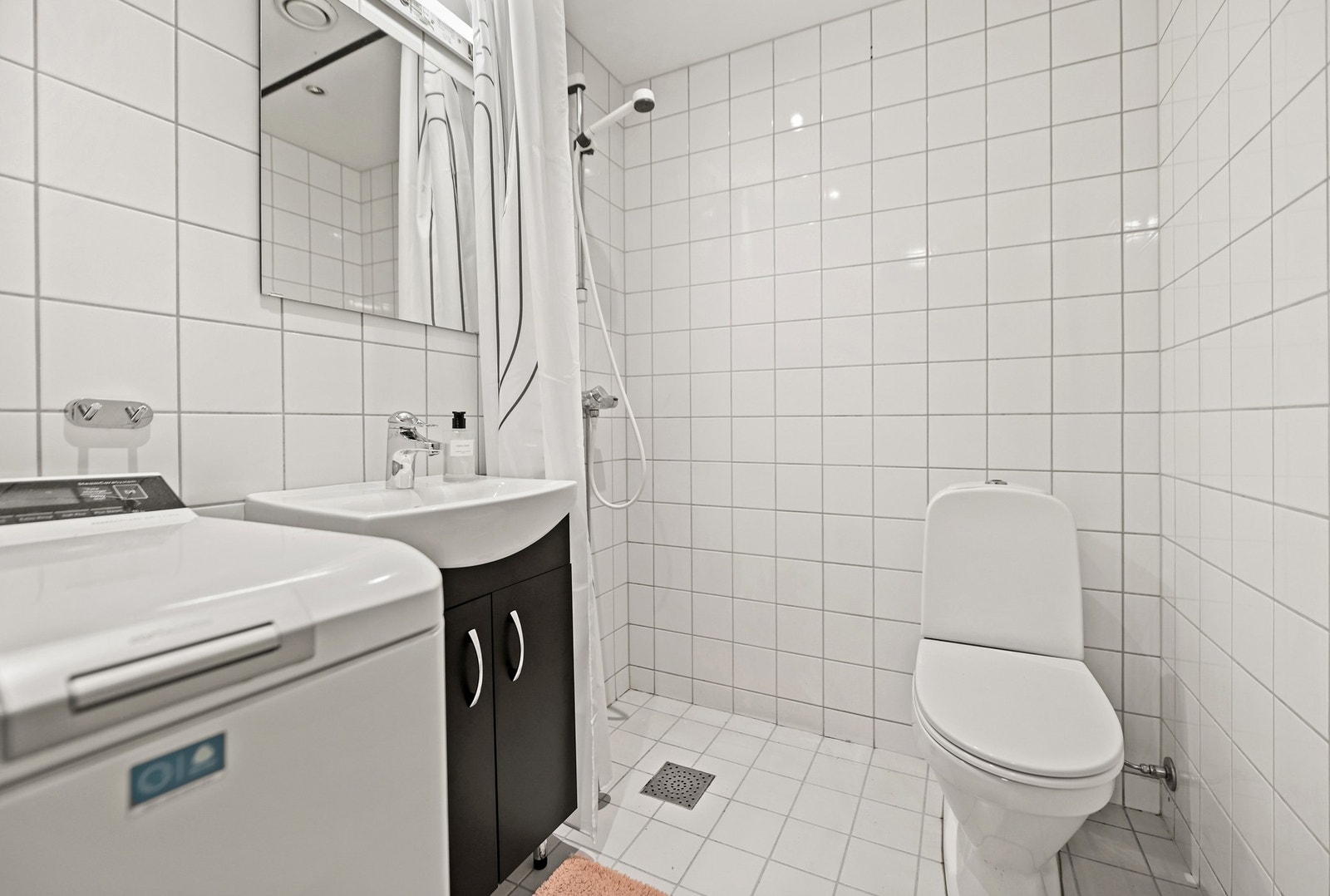 Leiligheten har et delikat bad. Innredningen er holdt i lyse og tidsriktige løsninger, gulvet er belagt med fliser og gulvvarme som gir behagelig, barfotvennlig varme. Badet er innredet med nedfelt servant (fra 2026), gulvfestet toalett, dusjhjørne og opp Galleribilde