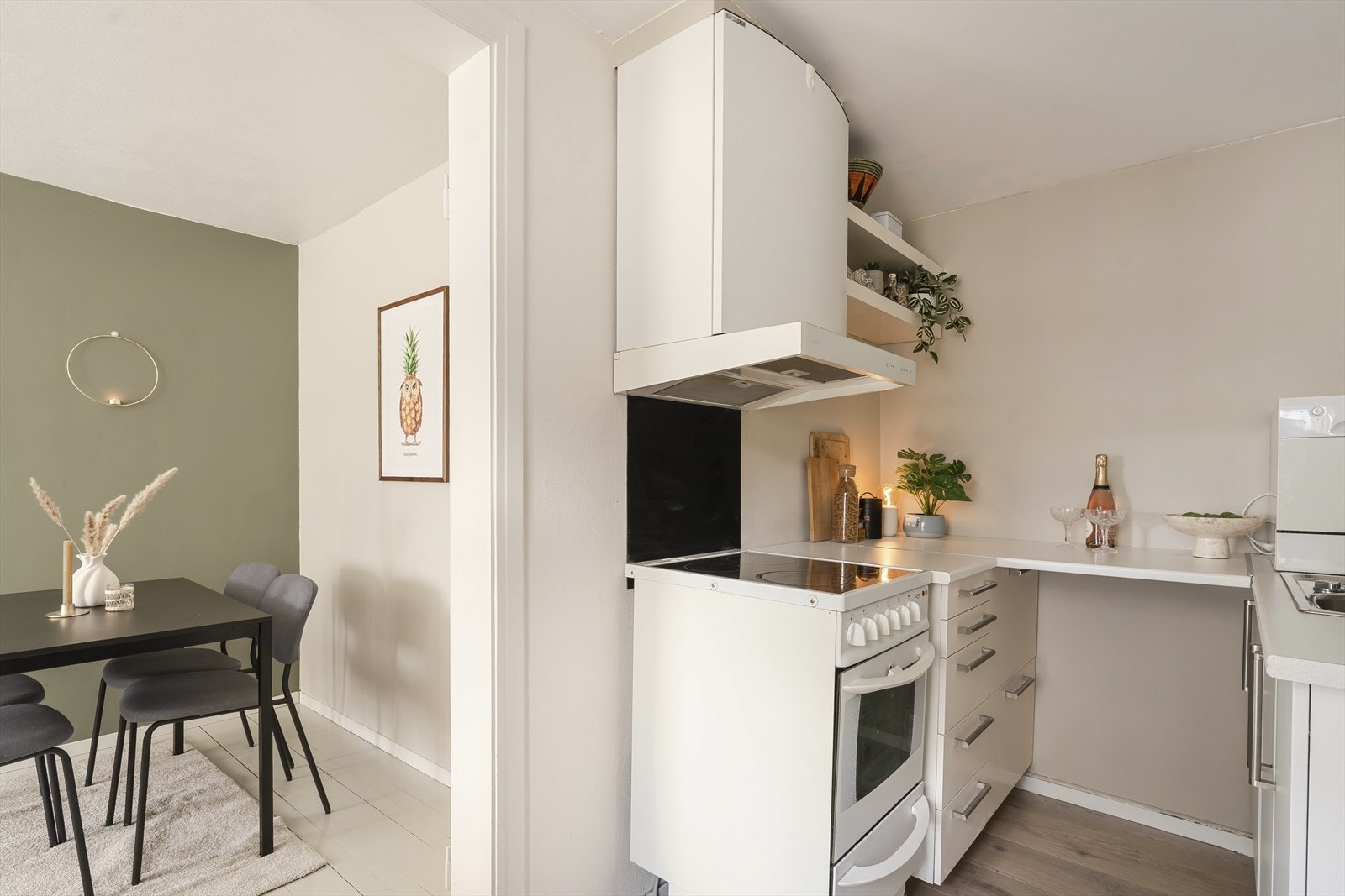Rommet er kompakt og funksjonelt innredet med hvite fronter, benkeplate med god arbeidsflate, oppvaskkum, komfyr og ventilator over stekesonen. Galleribilde
