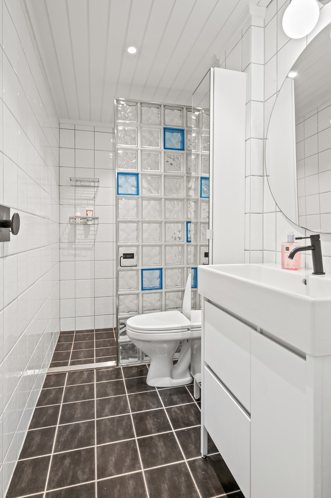 Badet har keramiske fliser på gulv og vegger, og er utstyrt med dusjnisje, servant med underskap og WC. Galleribilde