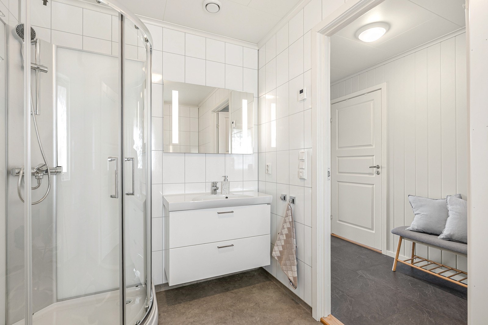 Badet innredet med toalett, baderomsinnredning med servant, speil med belysning og dusjkabinett. Galleribilde