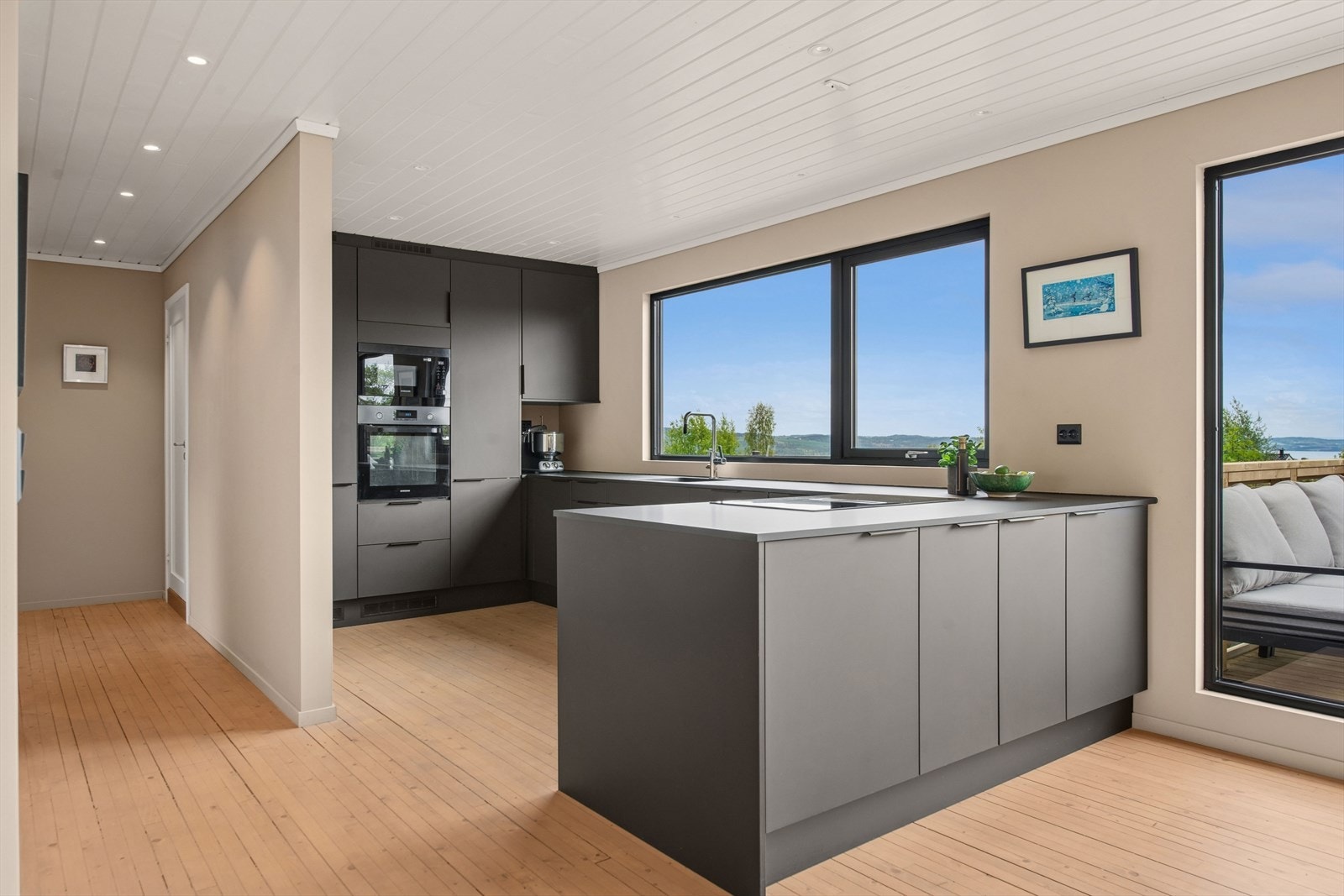 Kjøkkenet har en lekker og moderne innredning fra 2022 i MDF med mørke, slette fronter og mørk laminat benkeplate med nedfelt vaskekum. Galleribilde