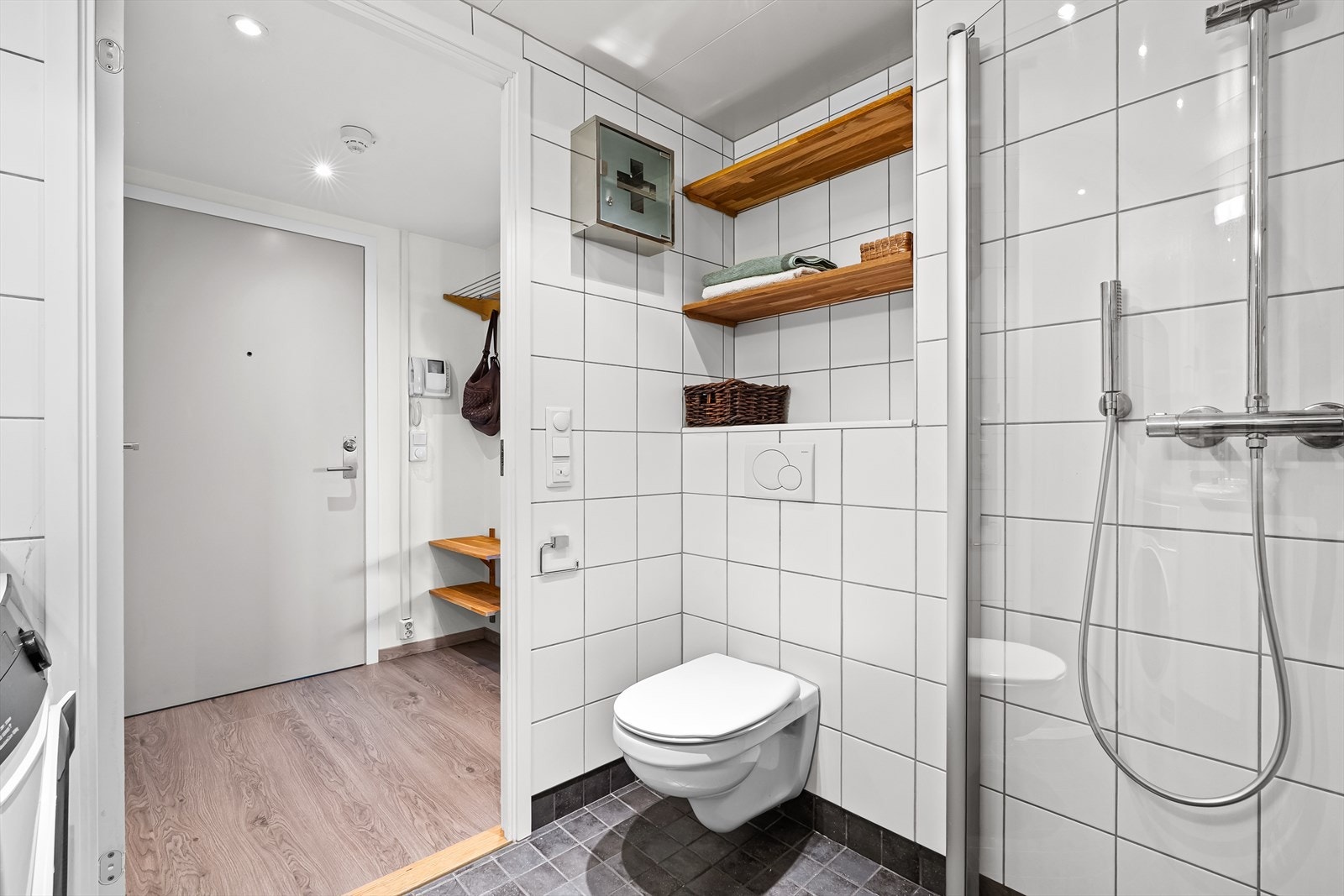Videre er badet innredet med vegghengt toalett, servant nedfelt i innredning, innfelt speil samt dusjhørne med to glassdører. Galleribilde