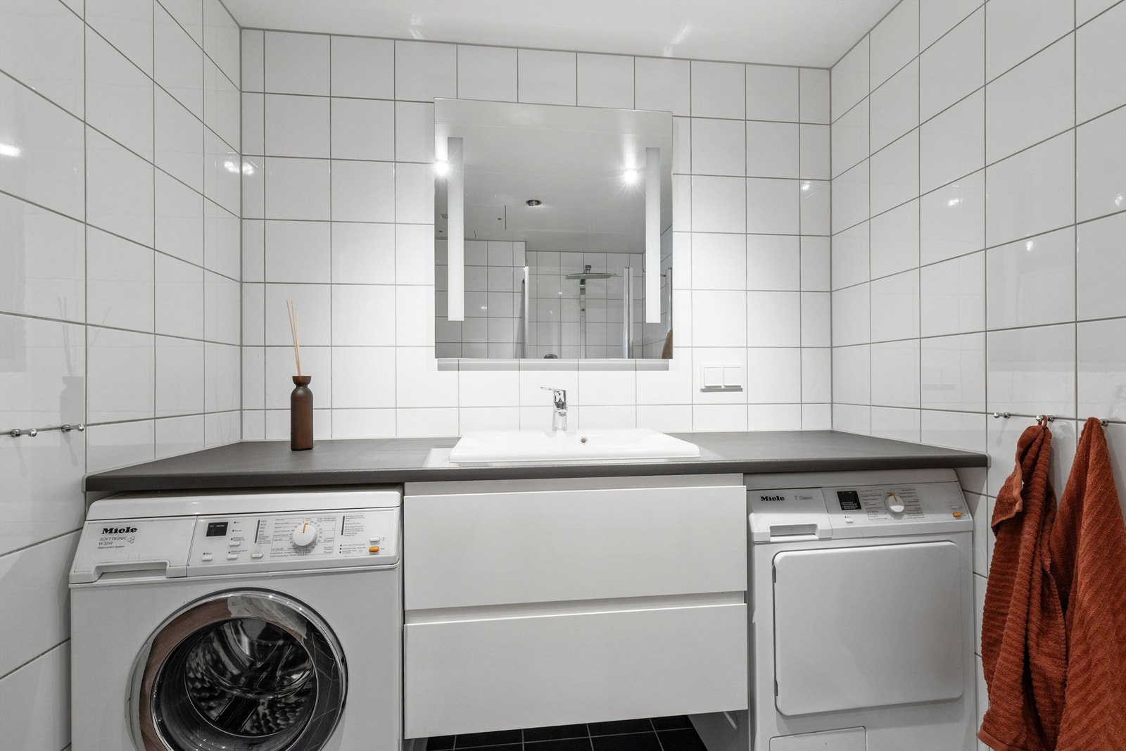 Badet er flislagt på vegger og gulv. Det er både plass og opplegg for vaskemaskin og tørketrommel i nisje innredning. Galleribilde