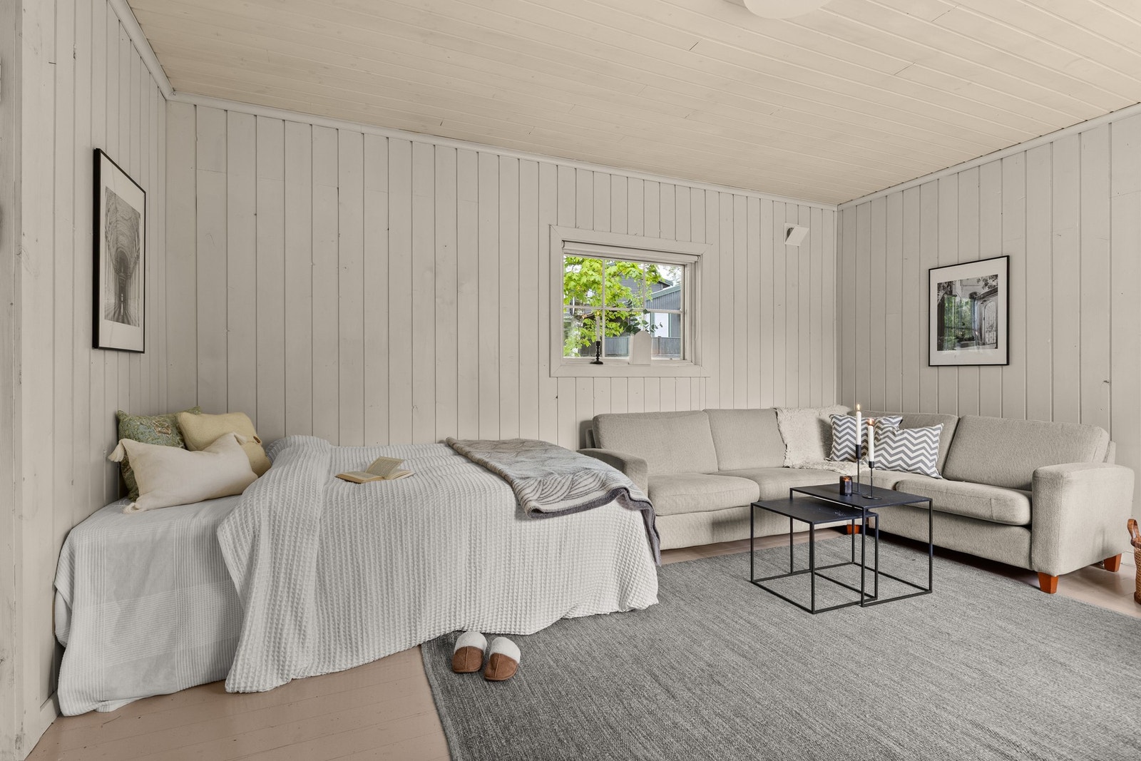 Rommet fremstår lyst og luftig med malte panelvegger og god plass til både sofa og seng. Galleribilde
