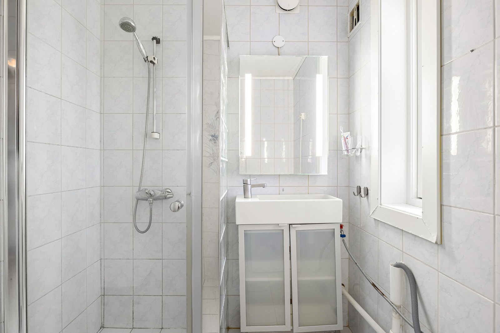 Badet er utstyrt med dusjnisje, servant med lagringsmuligheter i skap og moderne speil med integrert belysning. Galleribilde