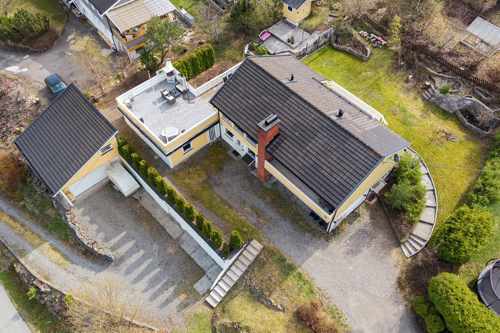 Det er to innkjøringer, en til garasjen og en til nivået der boligen er. Begge innkjørslene er delvis gruslagt. Hagen er opparbeidet med plenarealer, trær, busker og hekk. Galleribilde