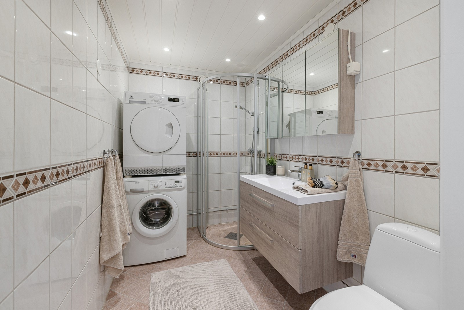 Pent, flislagt bad med varme i gulv og himling med downlights. Badet er innredet med servant med underskap, speilskap med belysning og stikkontakt samt dusjsone med dusjkabinett. Det er opplegg for vaskemaskin og tørketrommel. Galleribilde