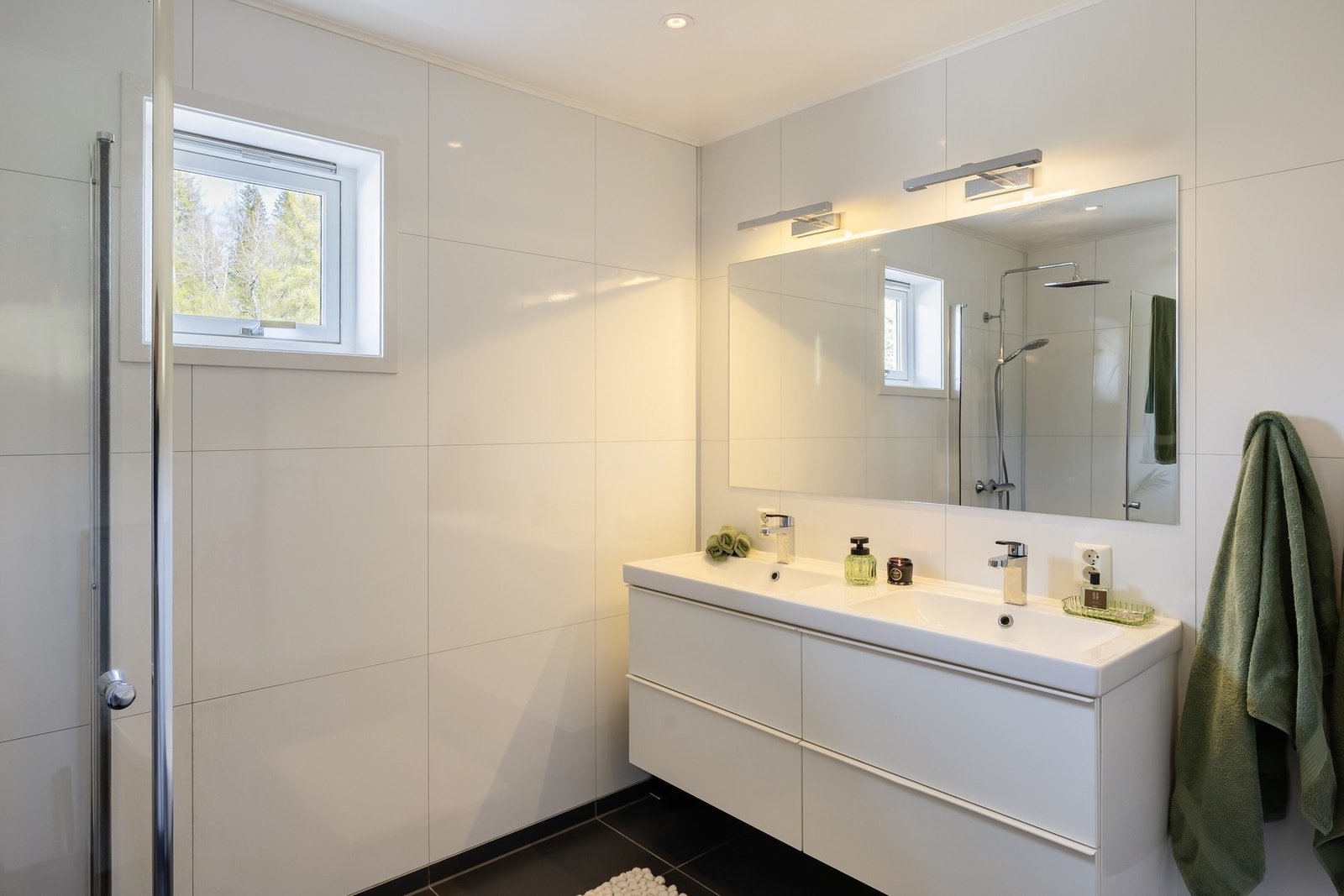 Badet har 60x60 fliser på gulv og baderomsplater på vegger. Her er baderominnredning med dobbel servant, høyskap, toalett og dusjhjørne med innfellbare glassdører. Galleribilde