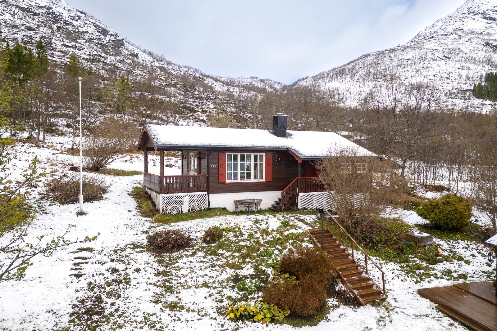 Pent oppbygd eiendom med gressplen, ulik beplantning og trapp ned til grillhytte Galleribilde