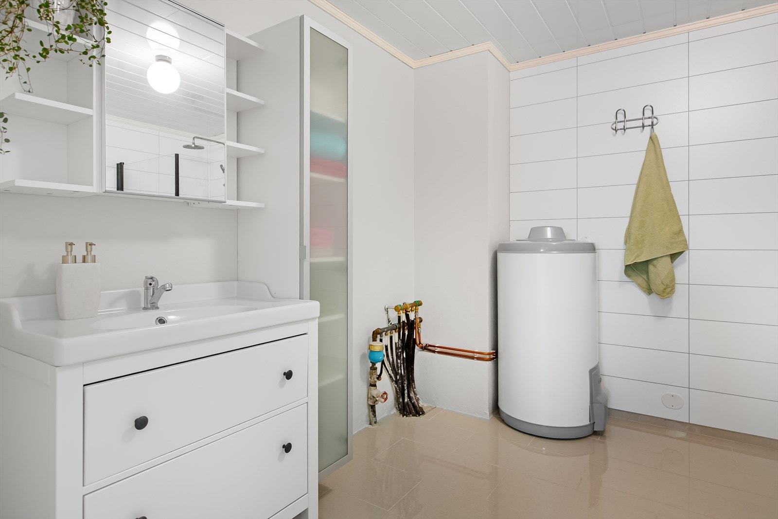 Badet er lyst og delikat med store fliser på gulv, og mindre mosaikkfliser i dusj. Hvit baderomsinnredning med store skuffer, heldekkende servant og overskap med speildør og hyller, samt et frittstående høyskap. Galleribilde