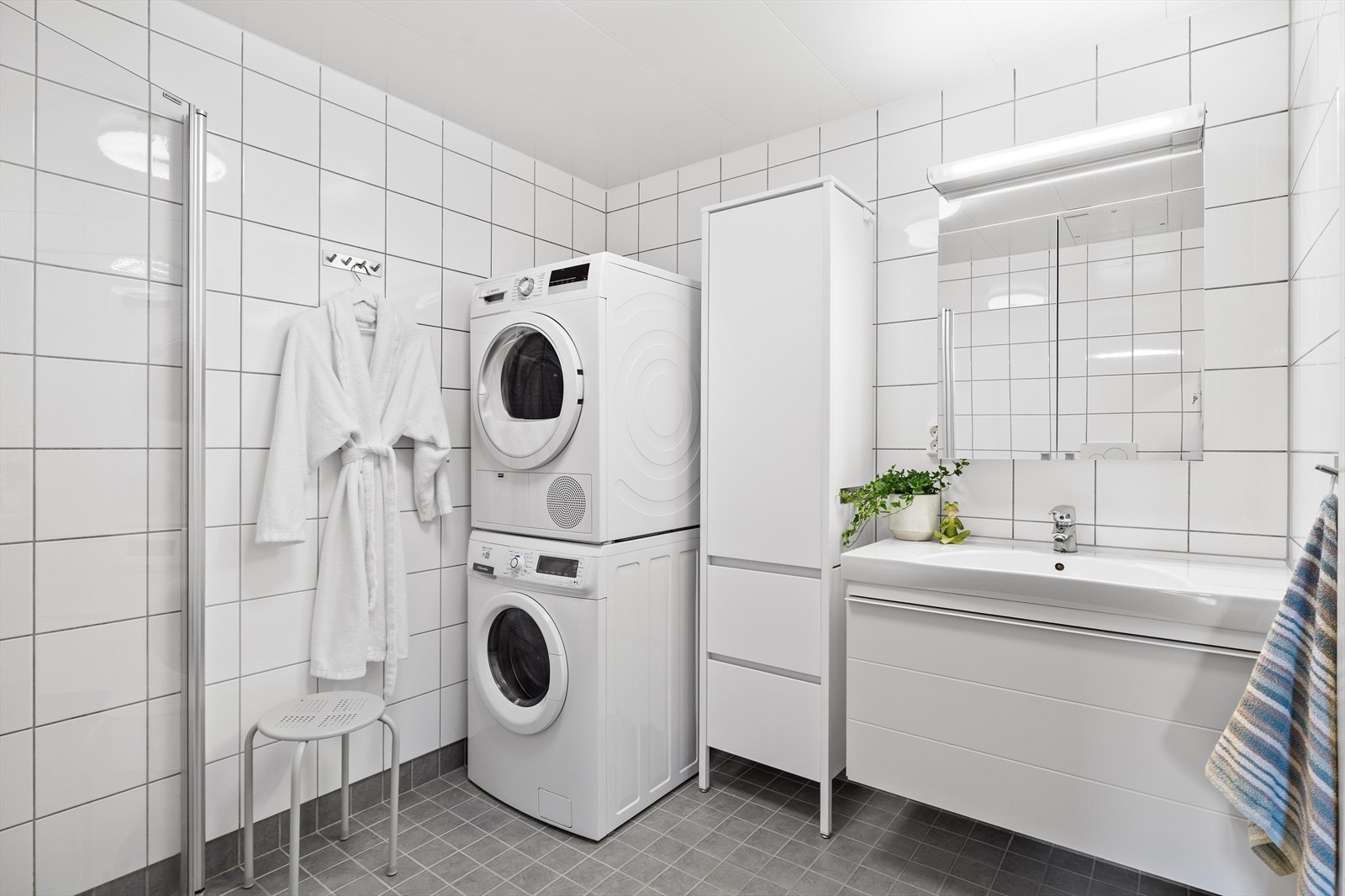 Badet har en praktisk planløsning som rommer både vaskemaskin og tørketrommel i søyle. Videre er badet utstyrt med innfellbare dusjdører, mekanisk avtrekk, toalett, servant i skap og et høyskap for oppbevaring av baderomsartikler. Galleribilde