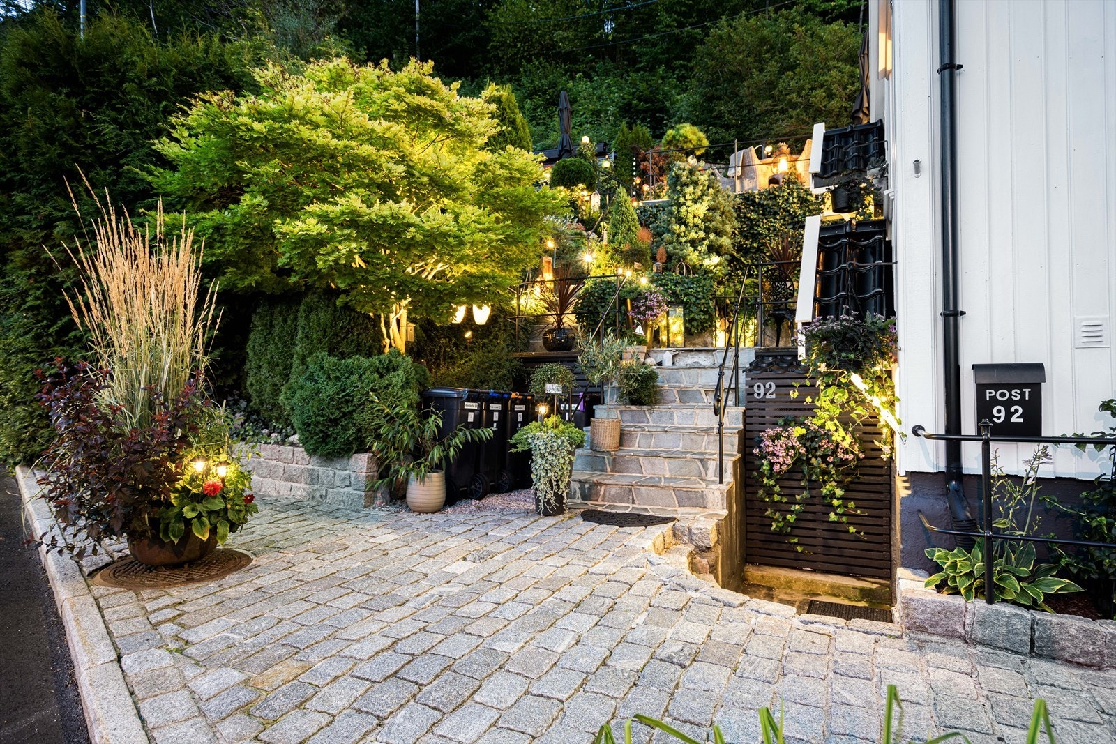 Fint med belegningsstein og flott hage med diverse trær, busker og blomster Galleribilde