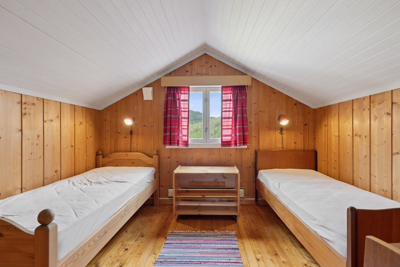 Bod innredet som soverom på loftet med trepanel på vegger og tak. Galleribilde