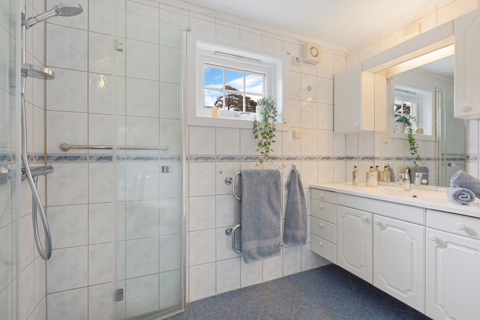 Badet er utstyrt med toalett, dusjhjørne med glassdører, samt baderomsinnredning med servant og speil. Galleribilde