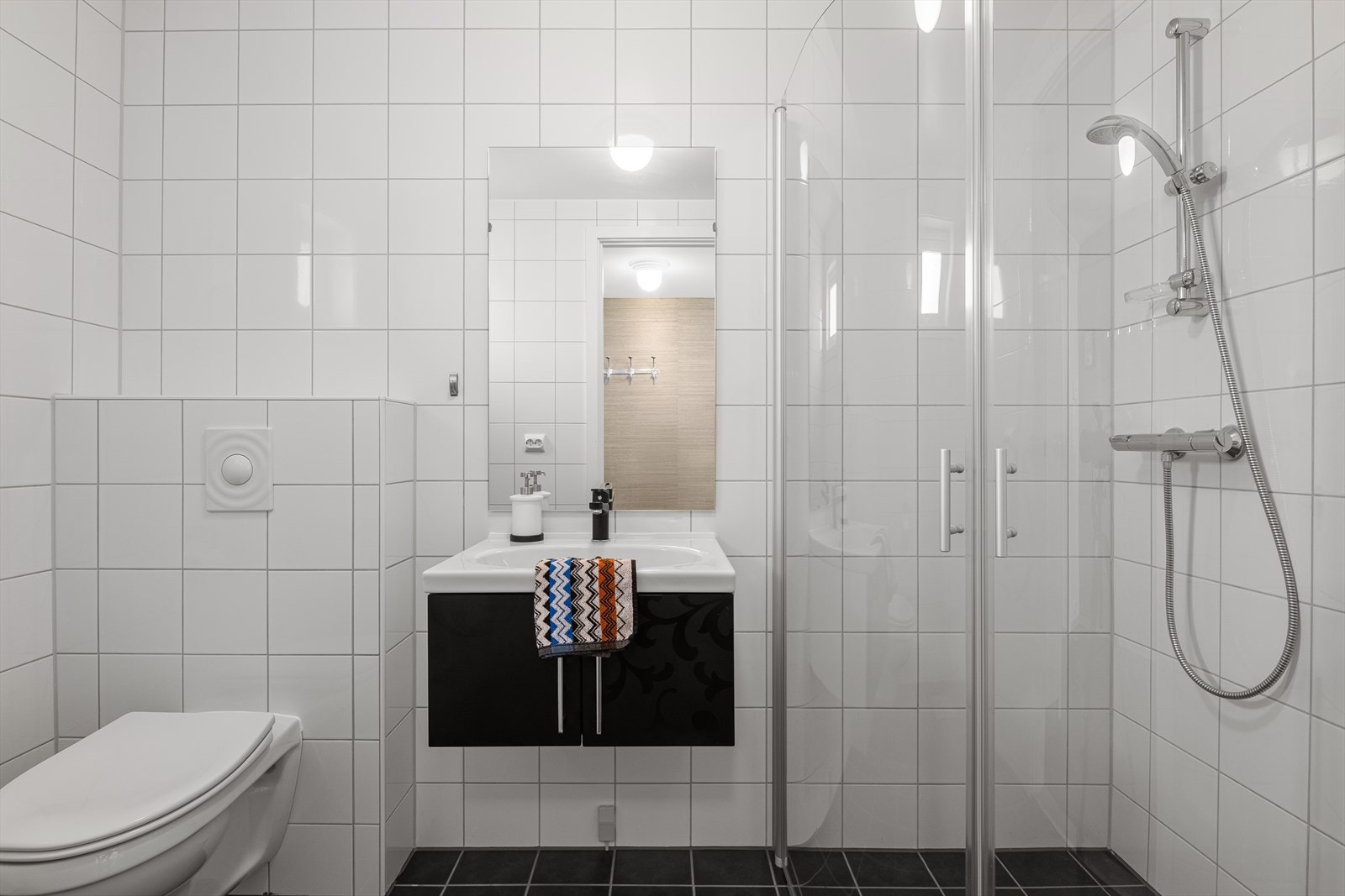 Badet i første etasje har flislagte overflater, veggmontert toalett, dusjhjørne og elektriske varmekabler i gulvet. Galleribilde