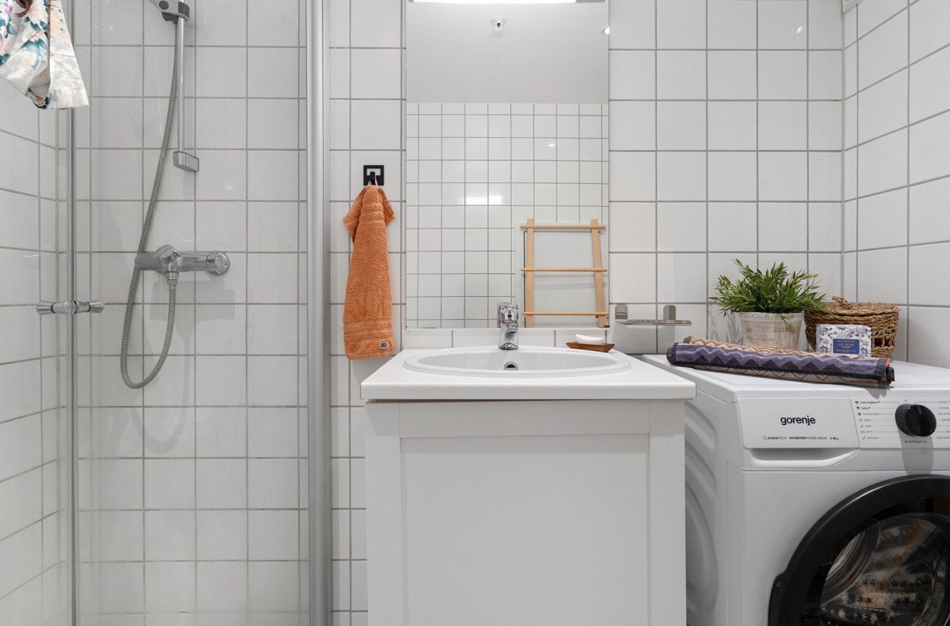 Dusjhjørne med buede glassdører og veggmontert hånddusj. Vegghengt toalett med synlig sisterne fra Geberit. Opplegg for vaskemaskin. Galleribilde