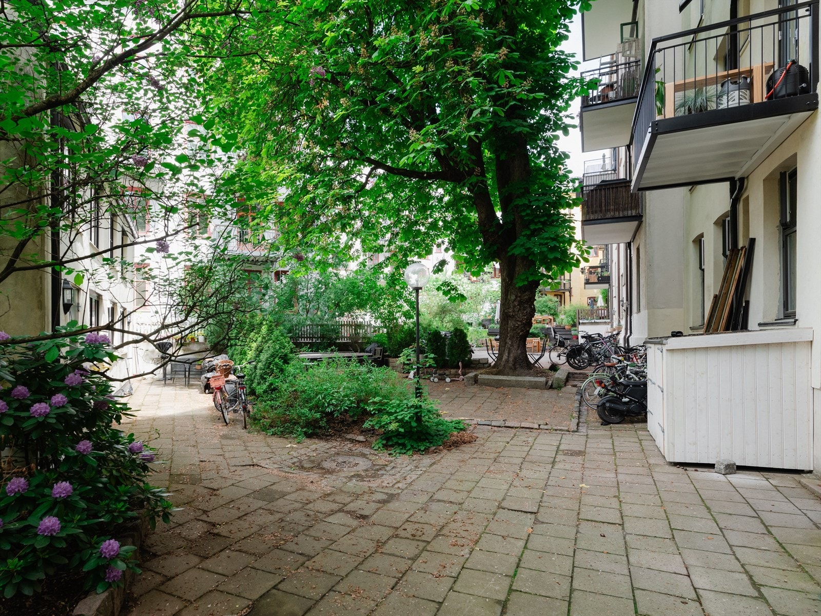Nydelig bakgård pent opparbeidet med hellestein, beplantning, blomster, trær og sittegrupper. Galleribilde
