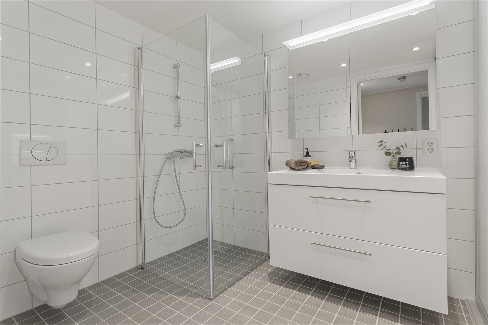 Badet er ca. 6,3 m² og inneholder servant med underskap, lys-speil med oppbevaringsmuligheter, veggehengt toalett, dusjgarnityr, downlights i himling. Galleribilde
