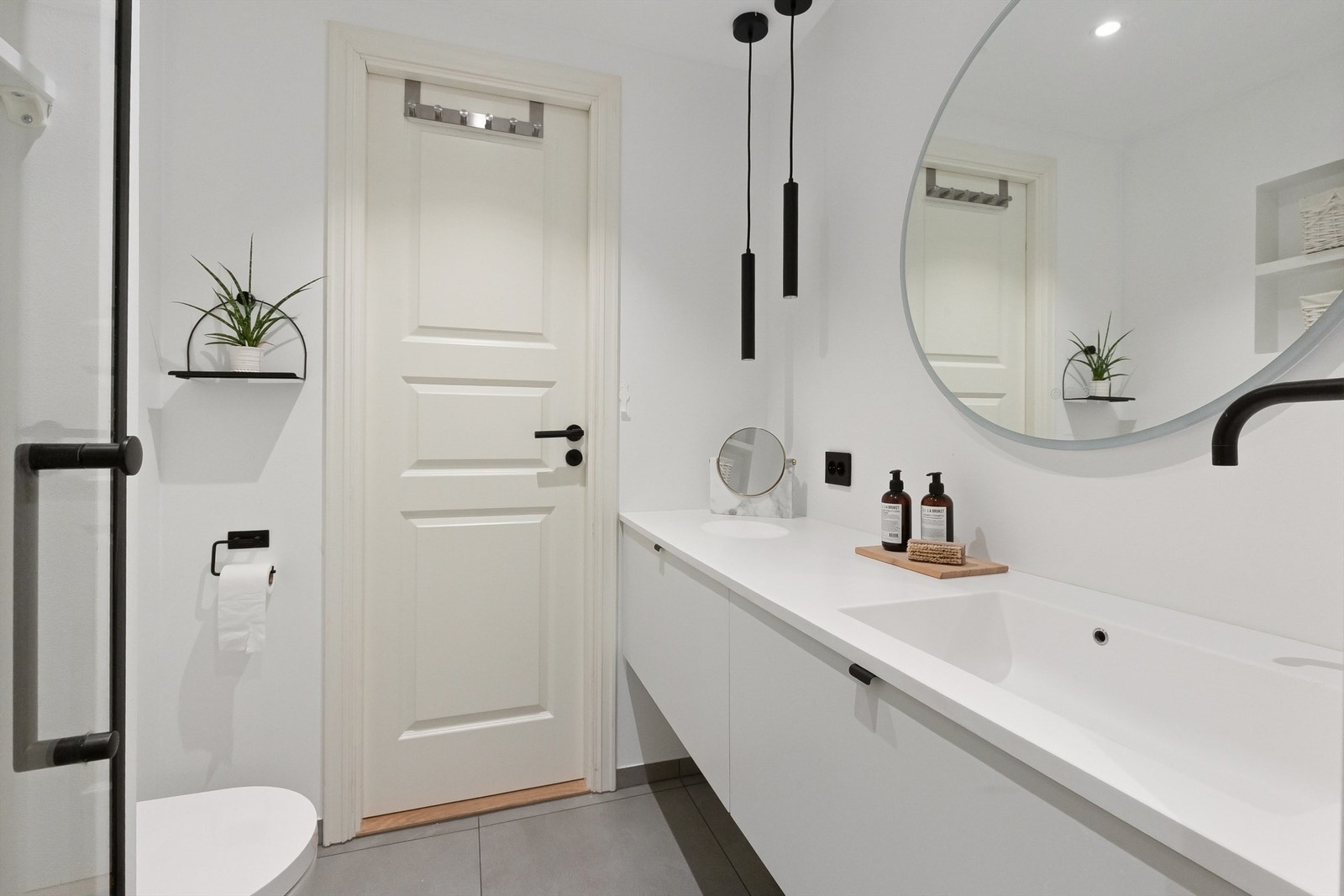 Lekkert baderom fra 2020 med gulvvarme og downlights. Det runde speilet har innebygd belysning. Godt med oppbevaring i benkeskap og integrerte hyllesystemer Galleribilde