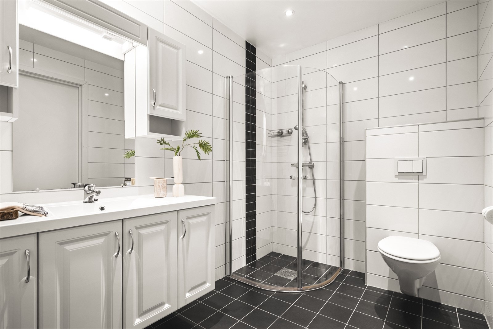 Badet er romslig og helfliset, utstyrt med nedfelt servant, dusjvegger, vegghengt toalett og opplegg for vaskemaskin. Galleribilde