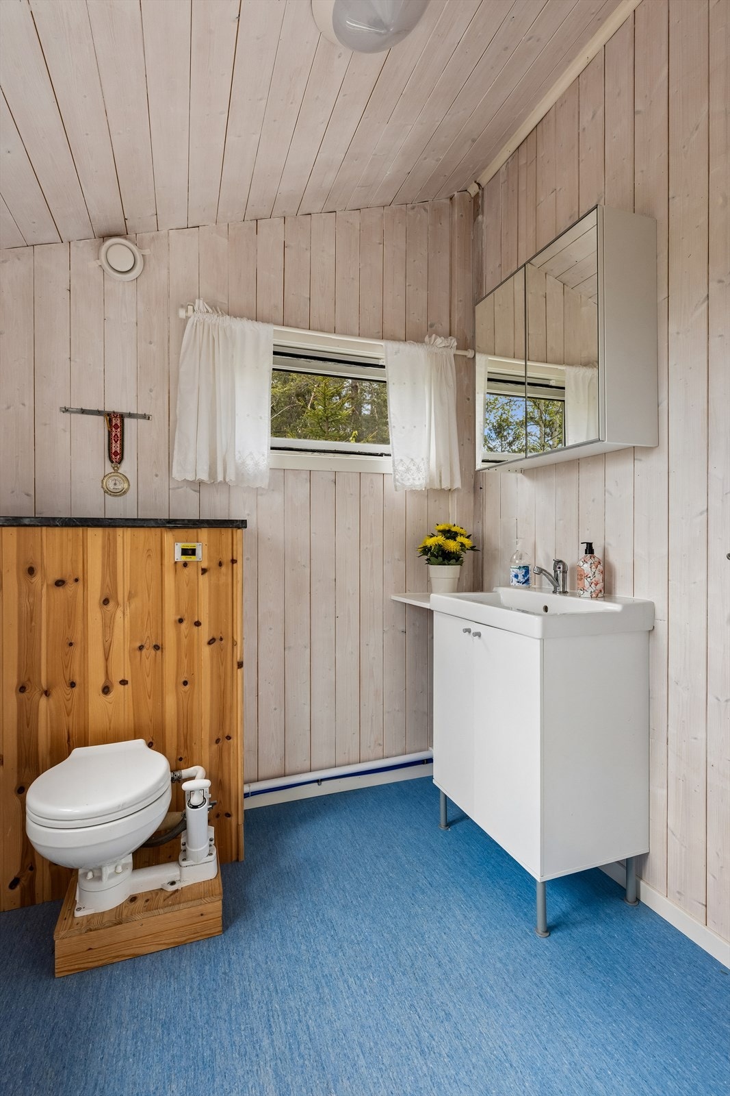 Badet er innredet med servant med underskap og har gulvbelegg og beiset trepanel på veggene. Galleribilde