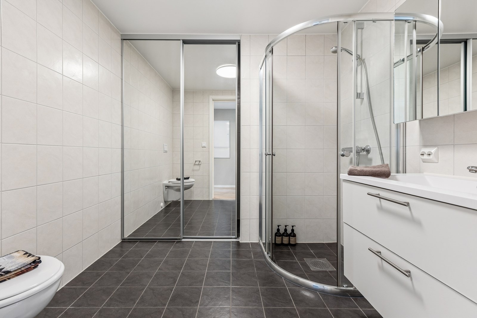 Rommet er funksjonelt innredet med stilren baderomsinnredning med nedfelt servant, vegghengt toalett og dusj med glassvegger. I tillegg er det praktisk opplegg for vaskemaskin. Galleribilde